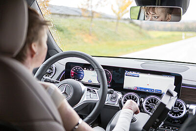 A young woman is sitting behind the wheel of her modified Paravan vehicle. Looking over her right shoulder, you can see that she is steering with a joystick on the right.