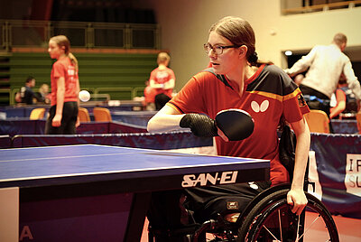Jana plays table tennis in a wheelchair wearing a red jersey.