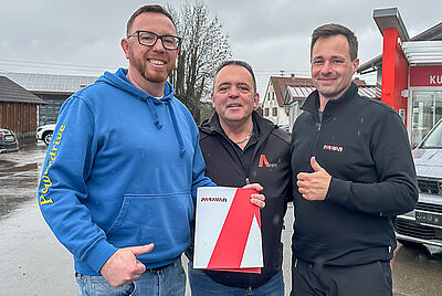Three men standing outdoors holding a PARAVAN folder; one of them wears a blue hoodie with “Powerdrive” lettering.