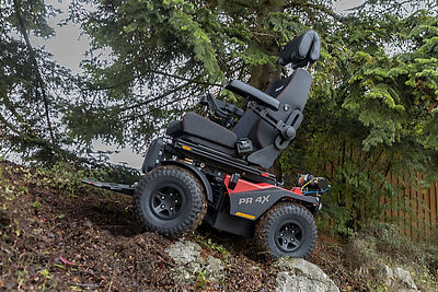 Geländegängiger Elektrorollstuhl Modell PR 4X auf unebenem Waldboden, ausgestattet mit großen Offroad-Reifen und stabiler Sitzkonstruktion.