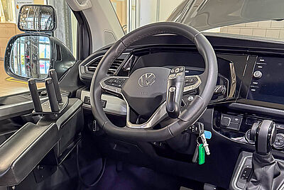 Interior view of a vehicle with a modified steering system, featuring extra grips on the door and an adapted steering wheel with integrated controls.