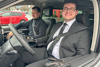 Young man with disability sitting behind the wheel of an adapted vehicle equipped with PARAVAN driving aids.