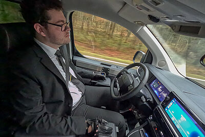 Driver with disability controlling an adapted vehicle with joystick steering while driving.