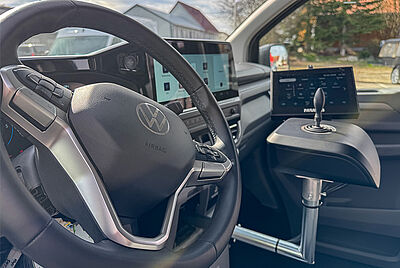 A close-up view of the interior of the new VW New Caravelle, showing a clear view of the steering wheel from the driver's side. Slightly out of focus in the background is a built-in Paravan joystick with a PARAVAN touch display.