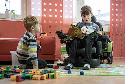Two children are playing together on the floor, one of them sitting in a lowered PR 25 children's wheelchair.
