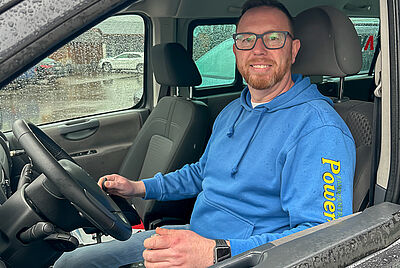 Man sitting in the driver’s seat of a van smiling at the camera.