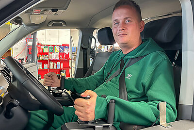 Philip sits in his wheelchair on the driver's side of his new vehicle and looks out the side window, his hands resting on the Space Drive input devices.