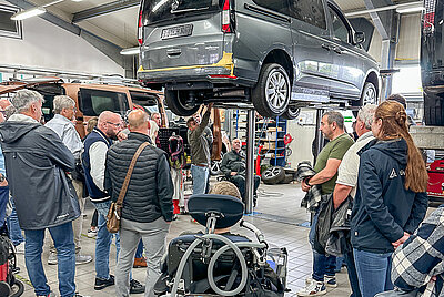 Technical tour or workshop visit at Paravan GmbH – visitors observing a van on a lift in the workshop.