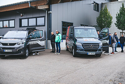 Several people examining or getting into mobility‑adapted vehicles of Paravan GmbH in an outdoor area.