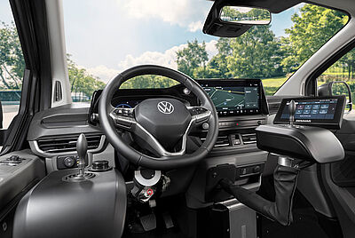 A close-up view of the interior of the new VW New Caravelle, showing a clear view of the steering wheel from the driver's side. Slightly out of focus in the background is a built-in Paravan joystick with a PARAVAN touch display.