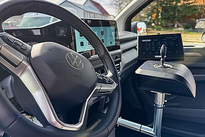 A close-up view of the interior of the new VW New Caravelle, showing a clear view of the steering wheel from the driver's side. Slightly out of focus in the background is a built-in Paravan joystick with a PARAVAN touch display.