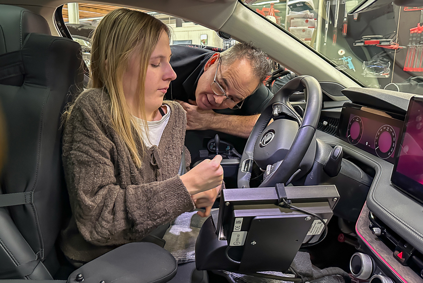 A young blonde woman is sitting in the driver's seat. A man is peering through the driver's side window. 