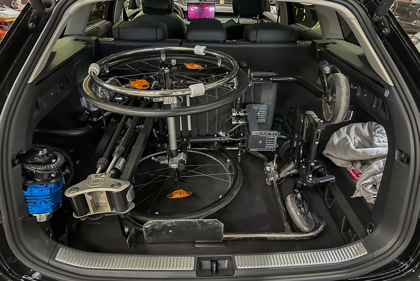 The trunk of a black car, with a Robot 3000 installed on the left side. There is also a power wheelchair in the trunk, which the Robot 3000 loaded into it. 