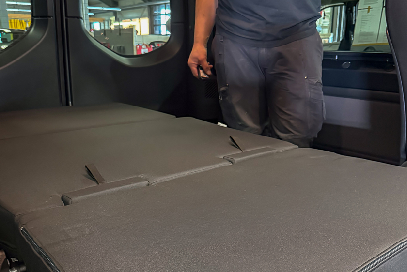 A sleeping area in a car, for resting and sleeping. Behind the sleeping area, you can still see the legs of a person standing there. 