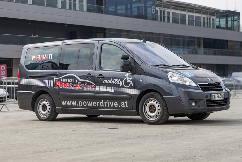 A gray car with Powerdrive Driving School decals and a Paravan logo on the rear side window.