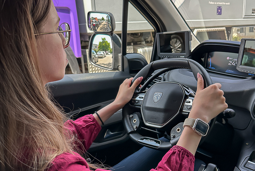 Looking over your right shoulder, you watch a young woman driving a car. Both of her hands are on the steering wheel.