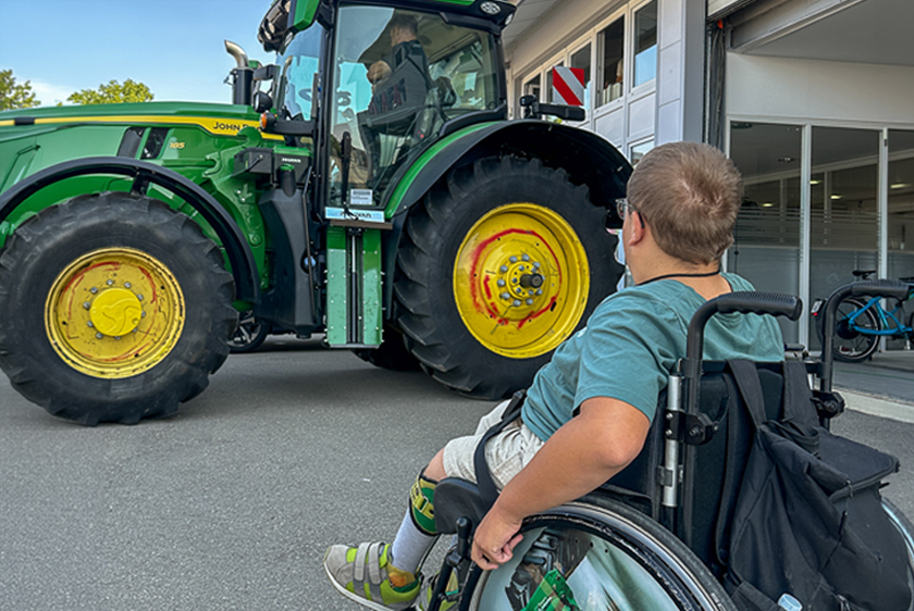 Wheelchair user looking at a John Deere tractor converted by PARAVAN outside the workshop.