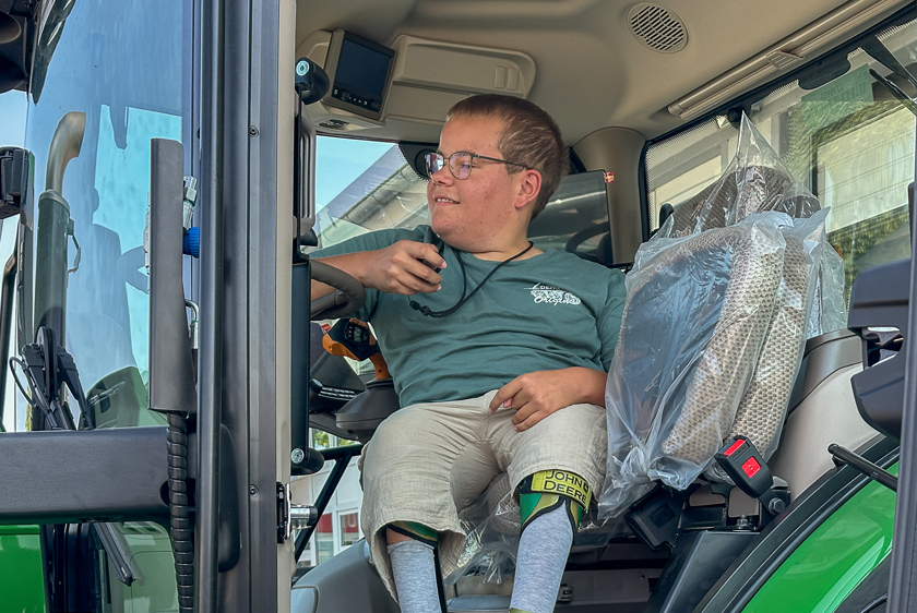 Young man sitting in the driver’s seat of an individually converted John Deere tractor with the cab door open.