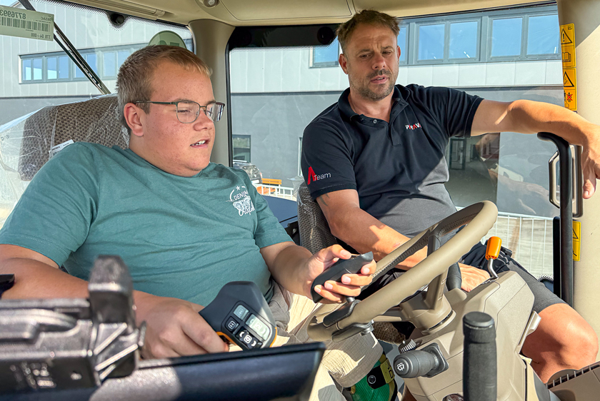 PARAVAN employee explains the adapted controls in the cockpit of a John Deere tractor to a young man.